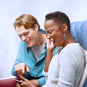 Couple sharing earbuds and watching content on a tablet inflight